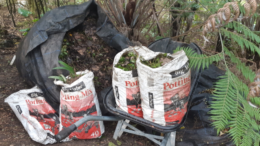 A black weed bag of composted weeds, garden sieve for grading compost, and a bag of potting mix